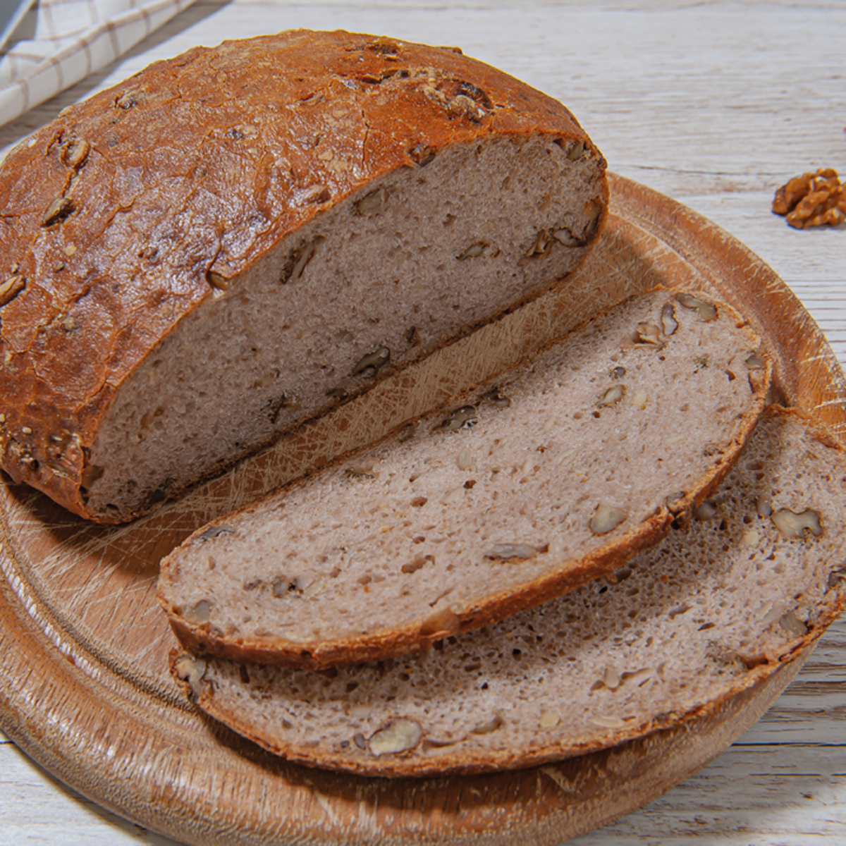 Ein Laib Brot mit Walnüssen, teilweise auf einem Holzbrett geschnitten. Die Kruste ist braun und knusprig, das Innere ist hell und weich.